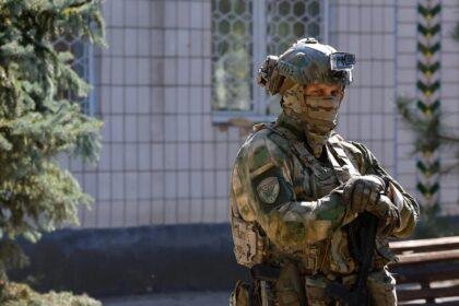 A Russian soldier in military camoflage and holding an assault rifle standing outside a school.