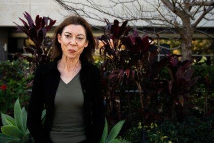 Alison Evans looks to the camera standing against a green, leafy background.