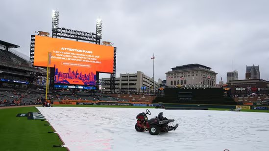 A tarp covers the field as rain falls while a message is seen on a video board alerting fans the start of Game 3 of baseball's American League Division Series between the Detroit Tigers and the Seattle Mariners will be delayed Tuesday, Oct. 7, 2025, in Detroit.(AP Photo/Ryan Sun)