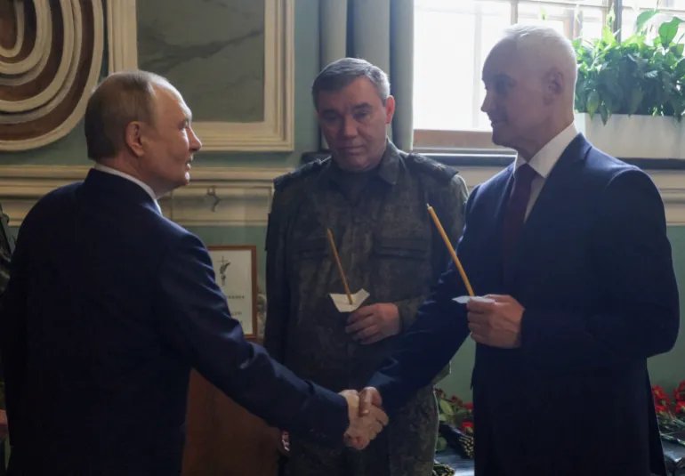 In this pool photograph distributed by the Russian state agency Sputnik, Russia's President Vladimir Putin shakes hands with Defence Minister Andrei Belousov as Chief of Staff Valery Gerasimov stands nearby while visiting the Peter and Paul Cathedral in Saint Petersburg on October 7, 2025. (Photo by Mikhail METZEL / POOL / AFP)