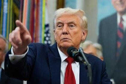 President Donald Trump wearing blue suit and a red tie while pointing at a reporter in the Oval Office